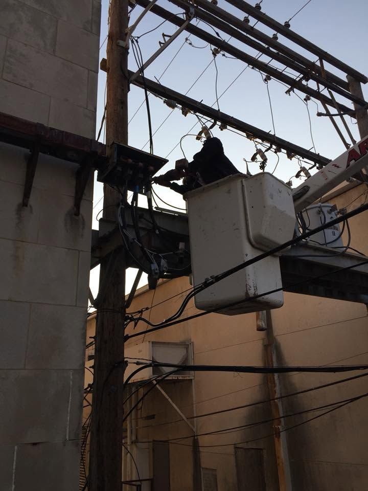 Worker on a utility pole repairing overhead power lines between buildings.