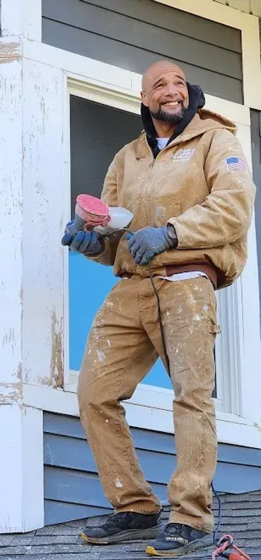 A man is standing on a porch holding a brush and smiling.