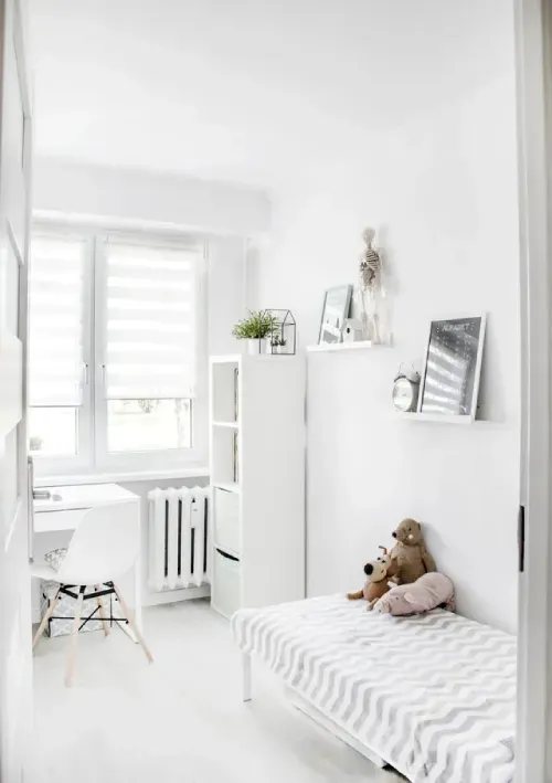 A white bedroom with a bed , desk , chair and window.
