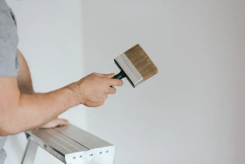 A man is standing on a ladder holding a paint brush.