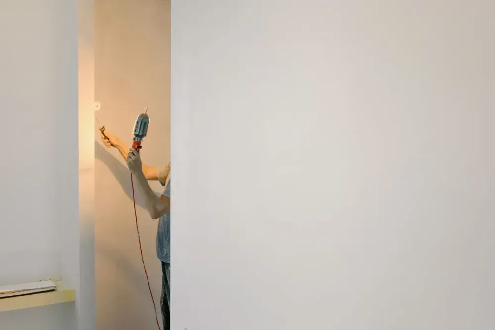A person is holding a drill in front of a white wall.