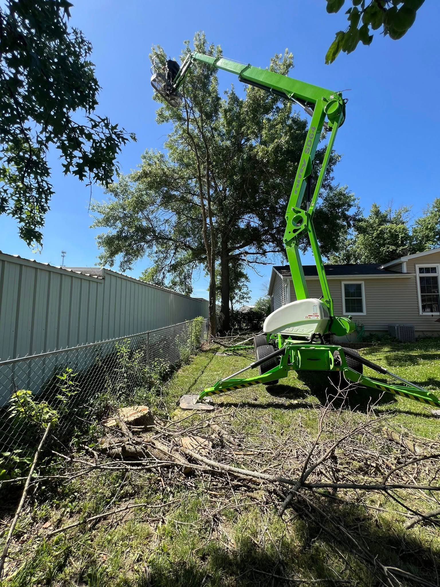 A green crane is cutting a tree in front of a house.