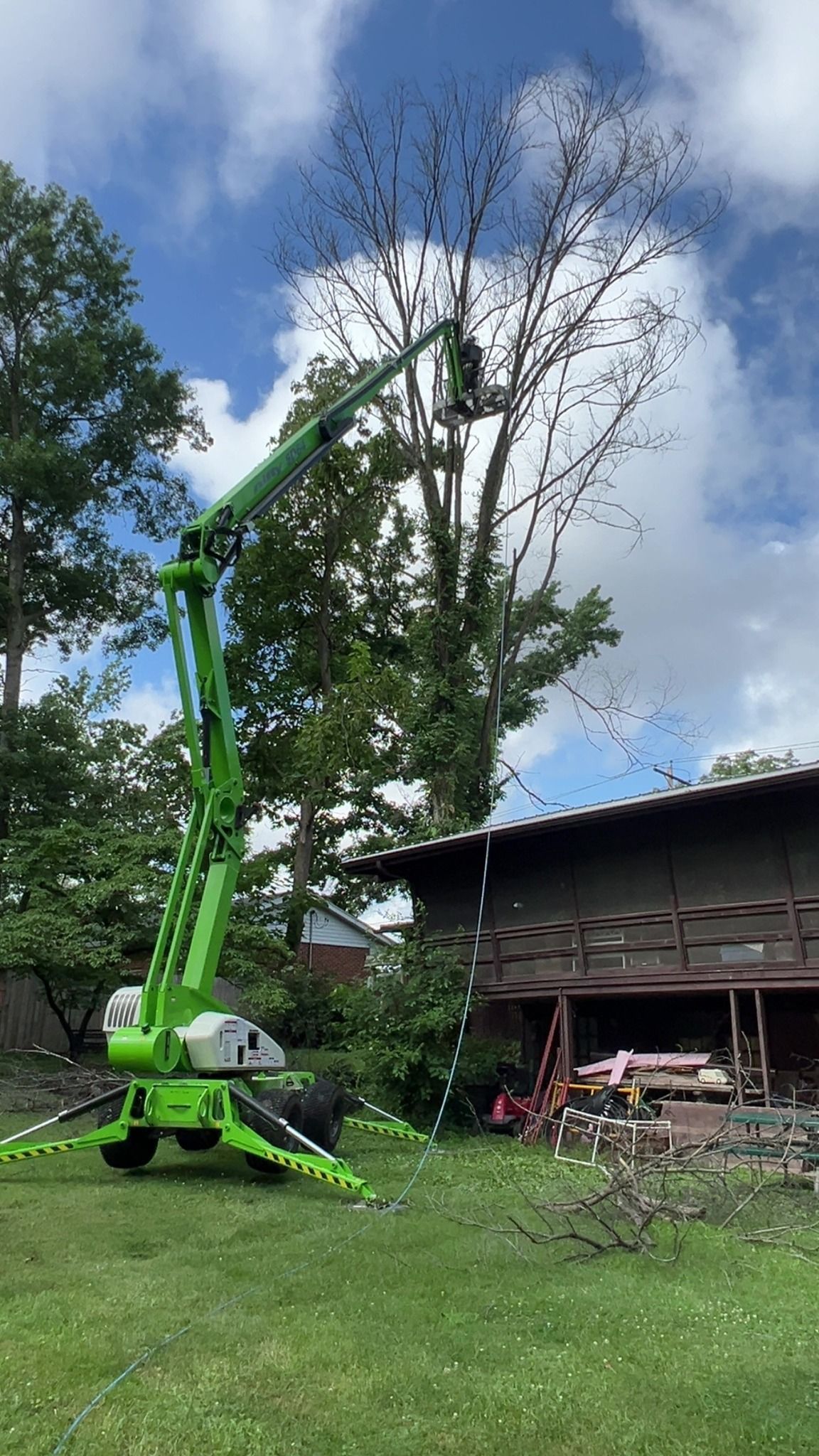 A green crane is cutting a tree in front of a house.