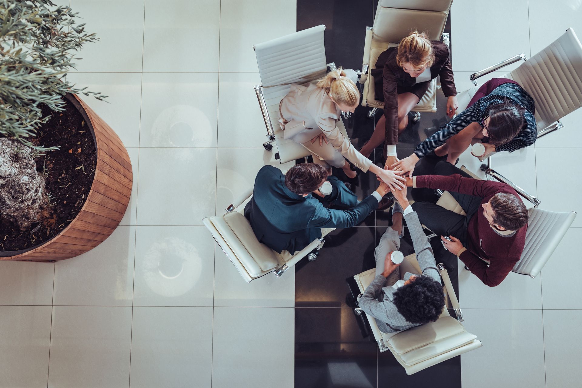 A group of people are sitting around a table putting their hands together.