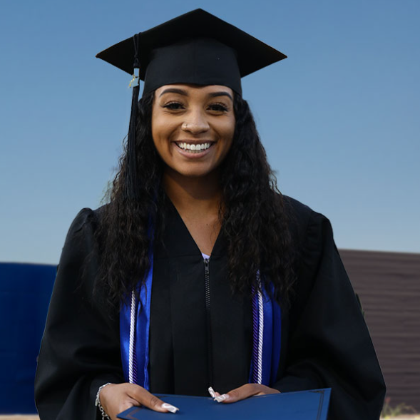 A woman in a graduation cap and gown is smiling and holding a diploma