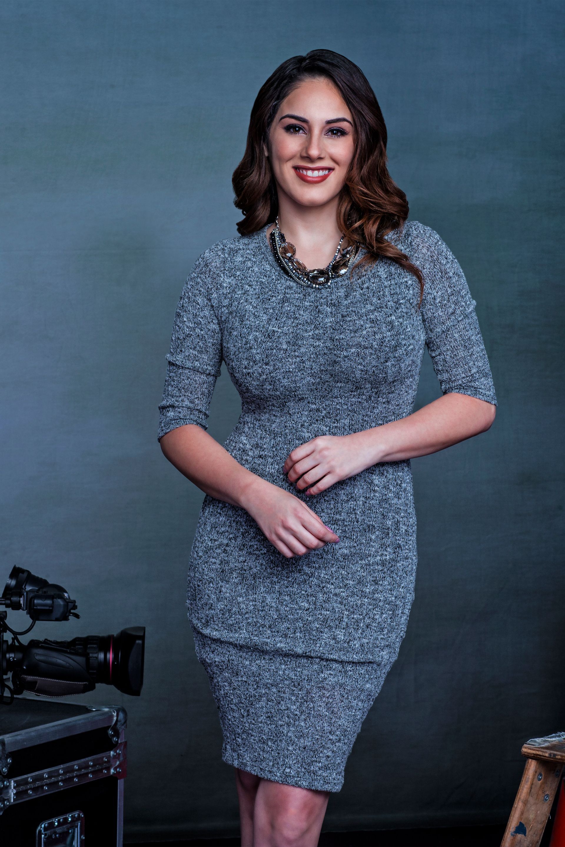 A woman in a gray dress is standing in front of a camera.