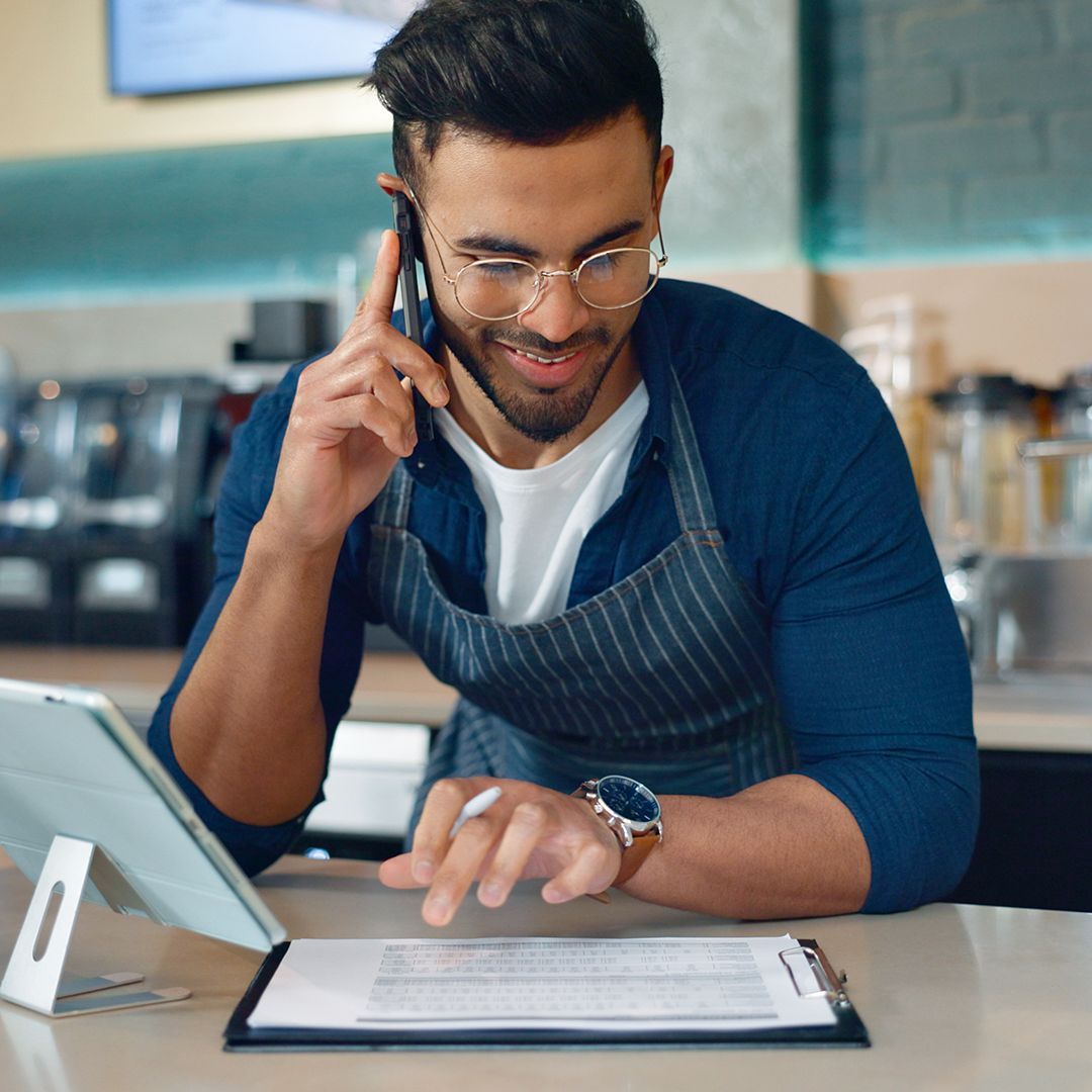 A man is talking on a cell phone while using a tablet