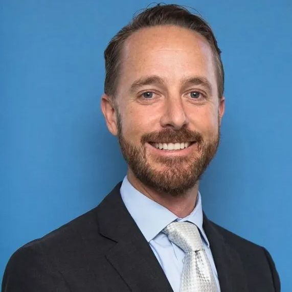 A man with a beard is wearing a suit and tie and smiling.