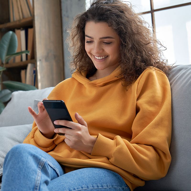 A woman is sitting on a couch looking at her cell phone.