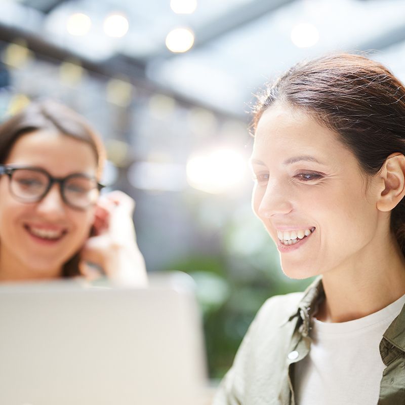 Two women are smiling while looking at a laptop computer.