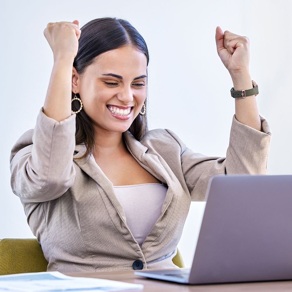 A woman is sitting in front of a laptop computer with her arms in the air.