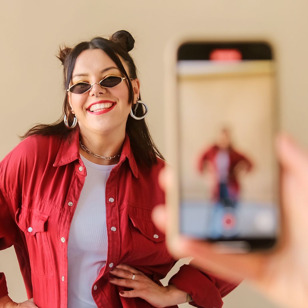 A woman in a red shirt is taking a picture of herself with a cell phone.