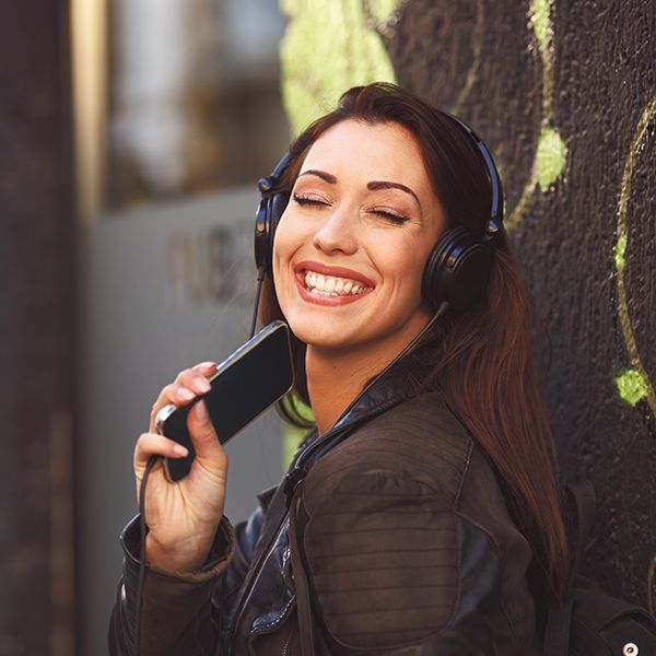 A woman wearing headphones is smiling while holding a cell phone