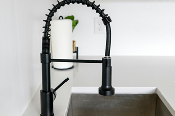 Black kitchen faucet with flexible spring and pull-down sprayer, white countertop.