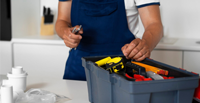 Person in a blue shirt and apron arranging tools in a gray toolbox on a workbench.