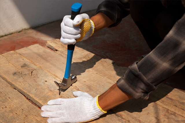 Hands in white gloves using a hammer to pull a nail from a wooden board.