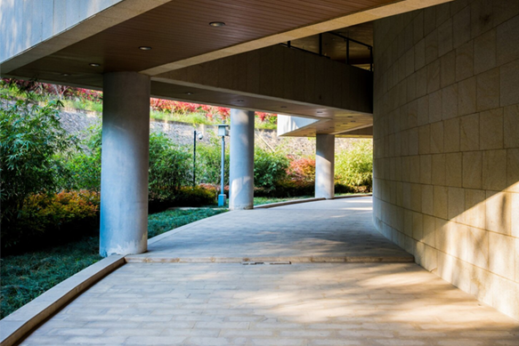 Curved covered walkway with concrete columns, warm sunlight, and greenery outside