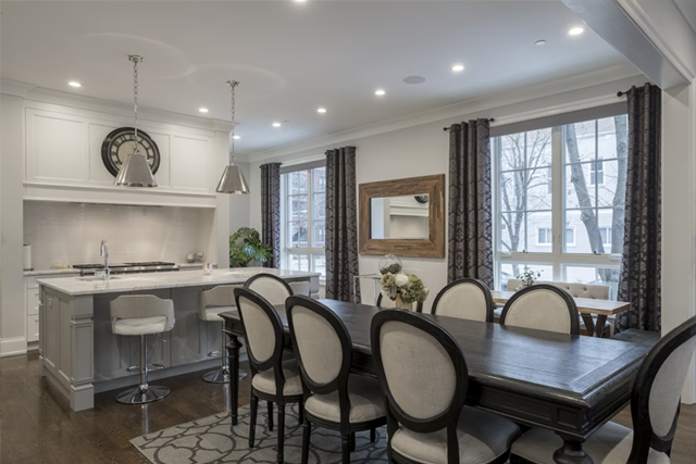 Bright dining room with dark table, upholstered chairs, kitchen island, and large windows in a modern home