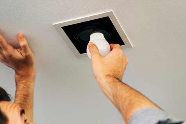 Hands installing a white light bulb into a recessed ceiling fixture.