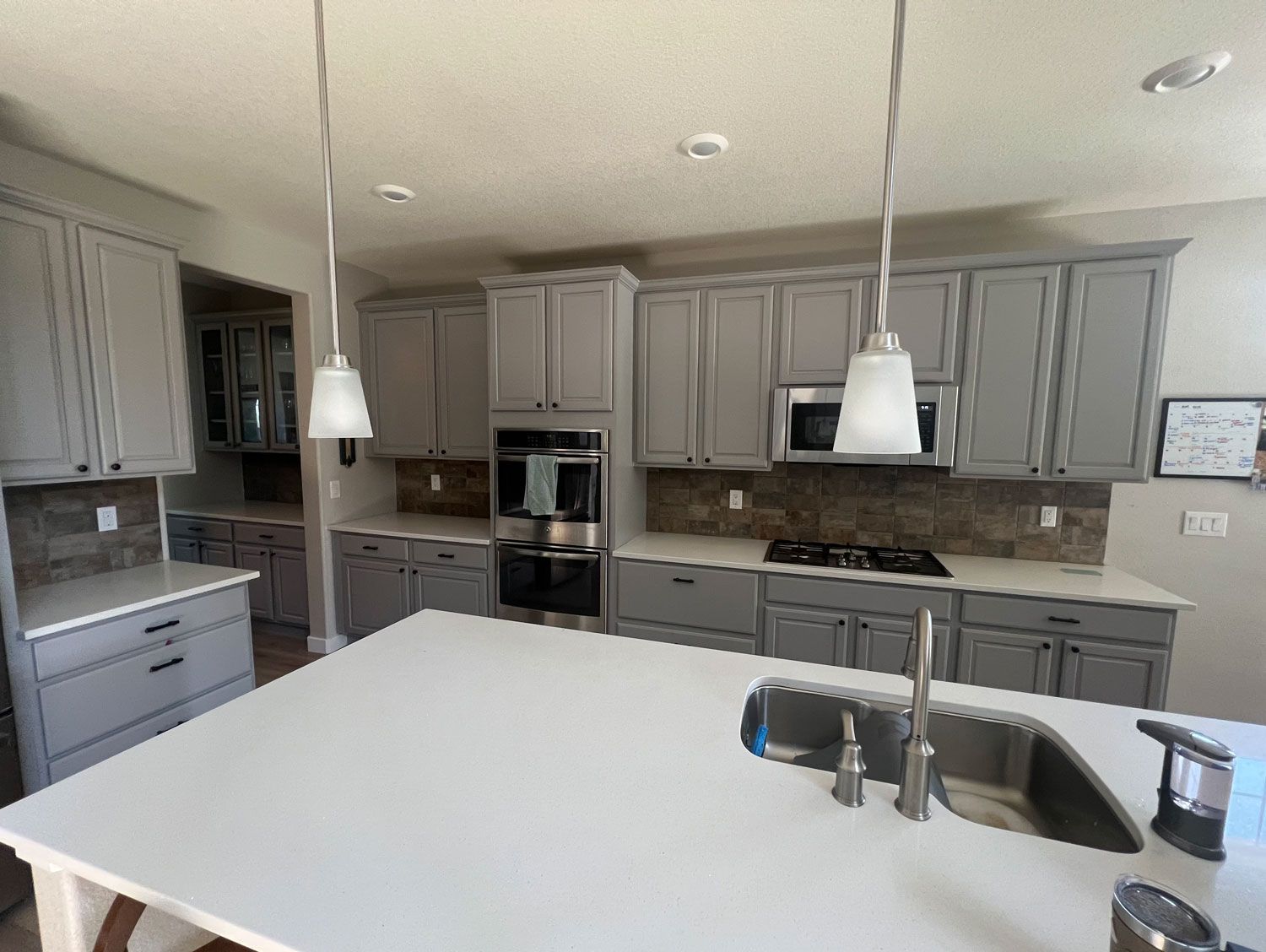 A kitchen with gray cabinets , stainless steel appliances , a sink , and a large island.