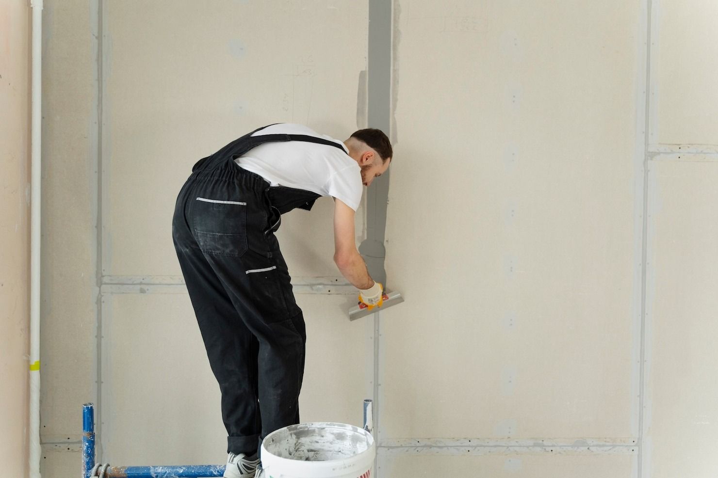 Person installing flooring, holding a plank covered with adhesive. Tools and bucket nearby.