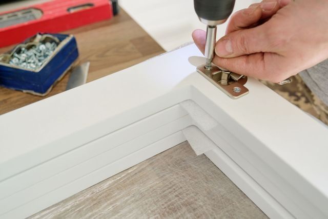 Person installing flooring, holding a plank covered with adhesive. Tools and bucket nearby.