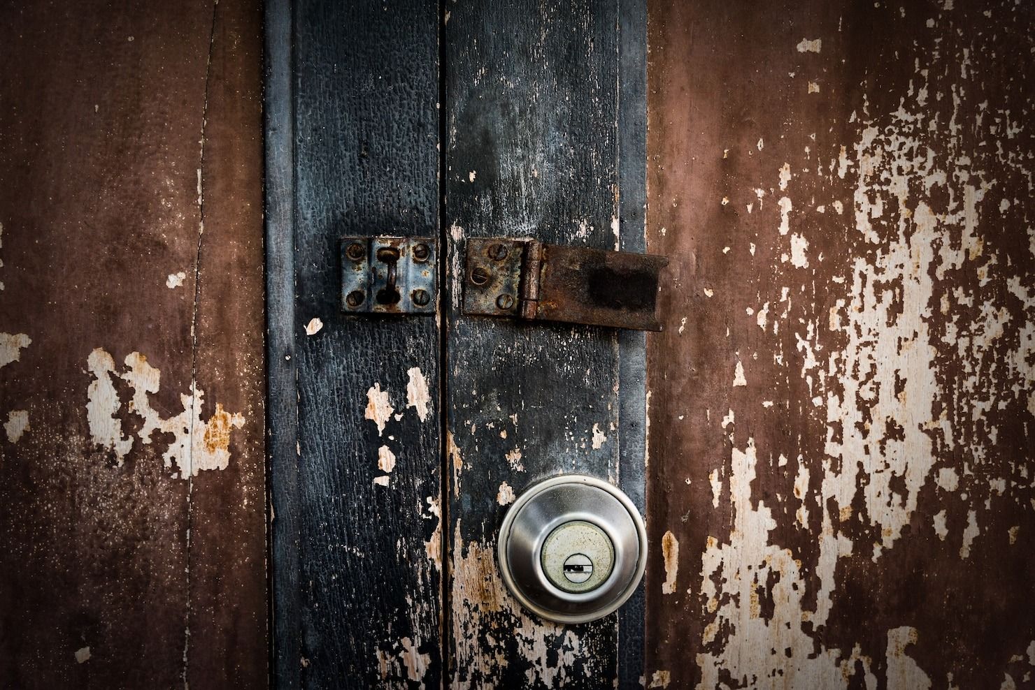 Rusty lock on weathered wooden door with peeling dark paint