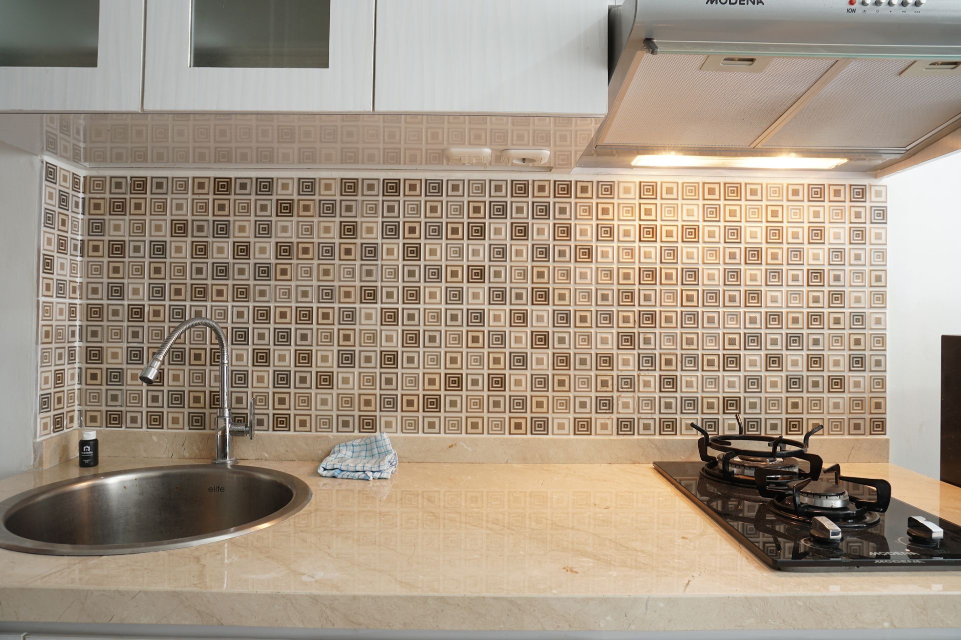 Modern kitchen countertop with sink, mosaic tile backsplash, and gas stove under white cabinets