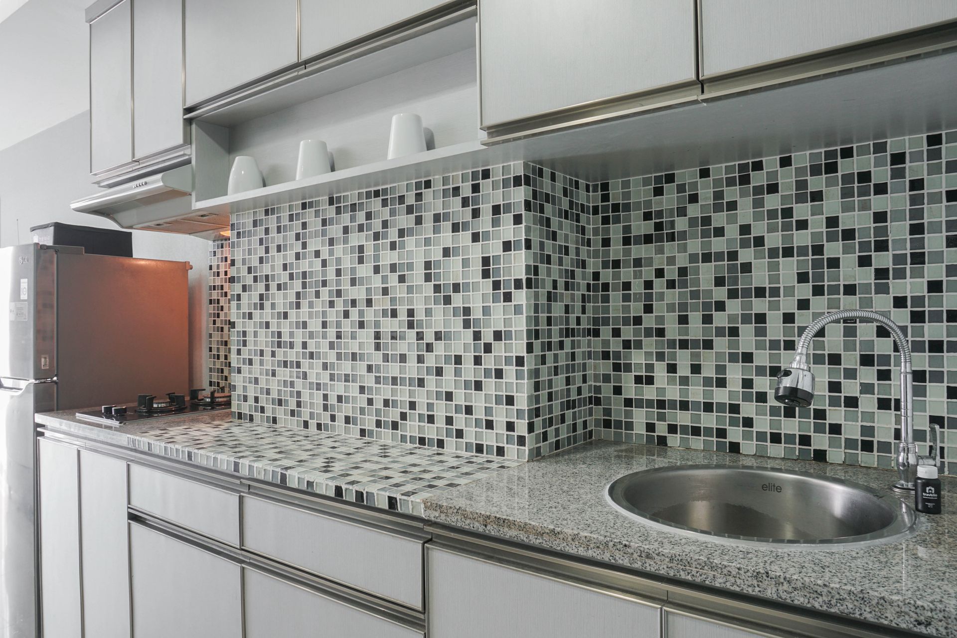 Modern kitchen with mosaic tile backsplash, granite countertop, sink, and open shelves with cups