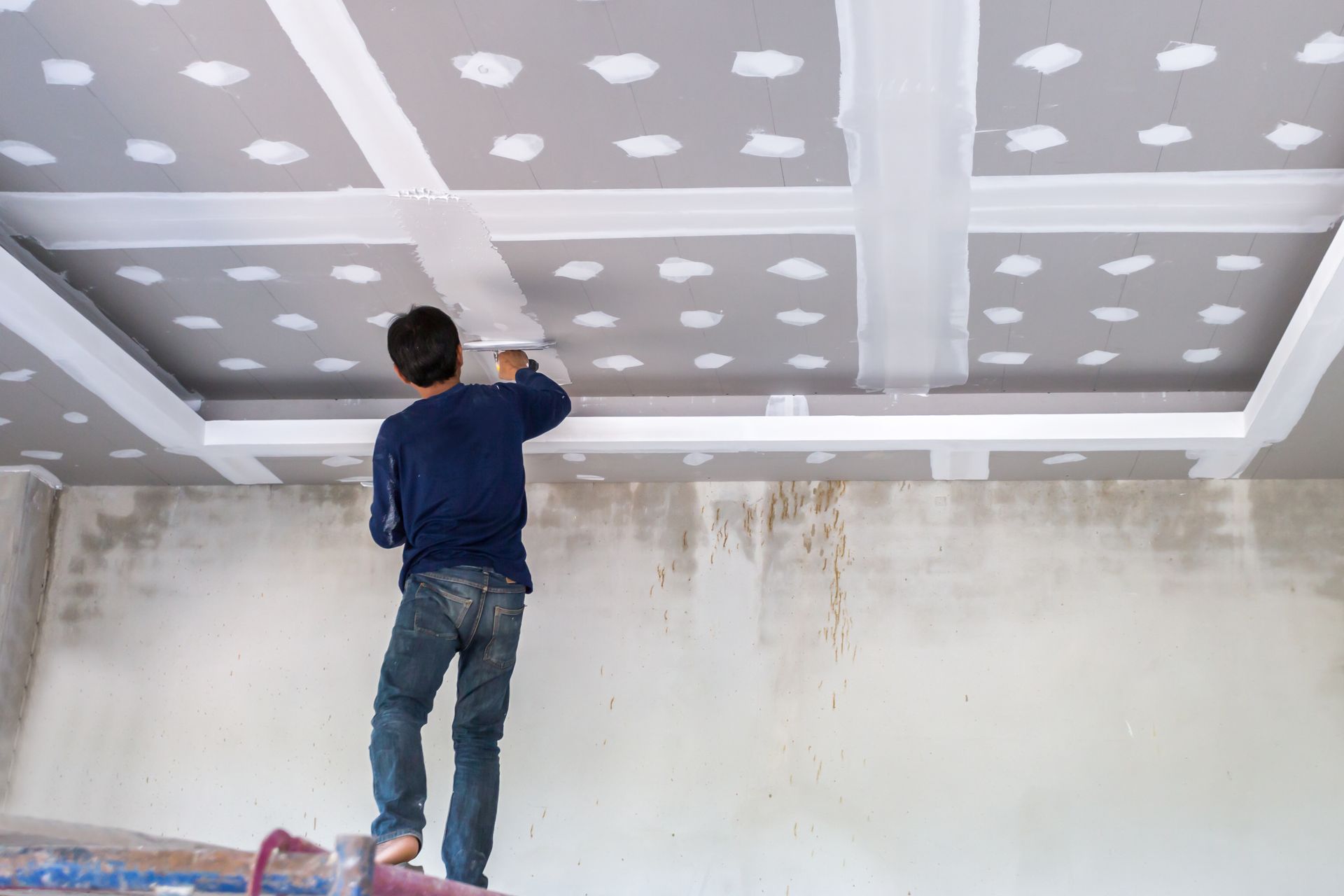 Worker painting a ceiling drywall seam in a room under renovation
