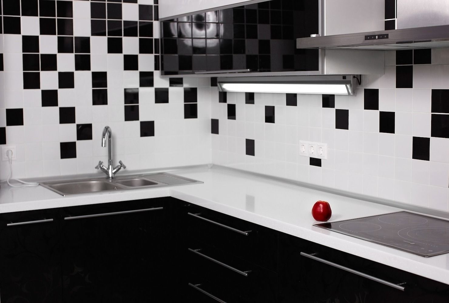 Modern kitchen with black-and-white tiled backsplash, black cabinets, and a red apple on the counter