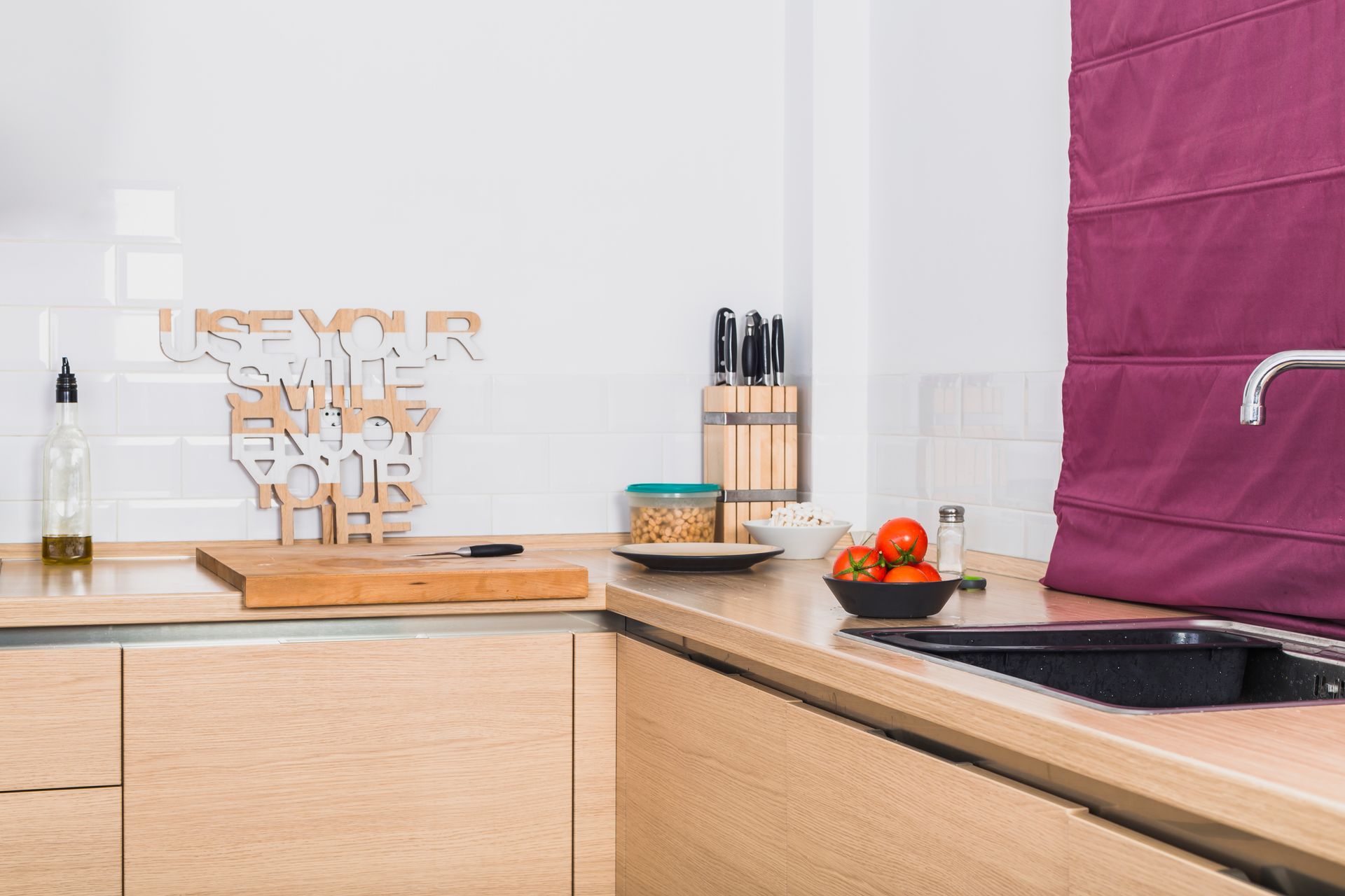 Modern kitchen counter with wood cabinets, sink, fruit bowl, spice rack, and magenta backsplash cover