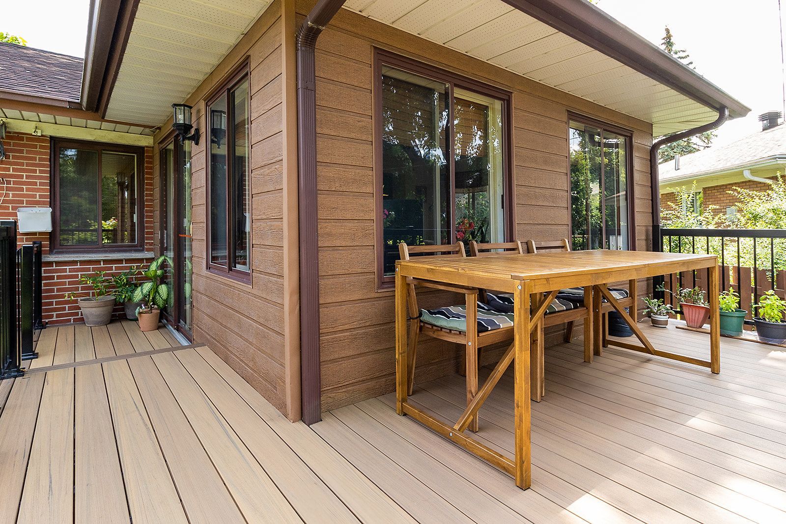 Terrasse en bois avec bardage marron, table à manger et portes coulissantes en verre.