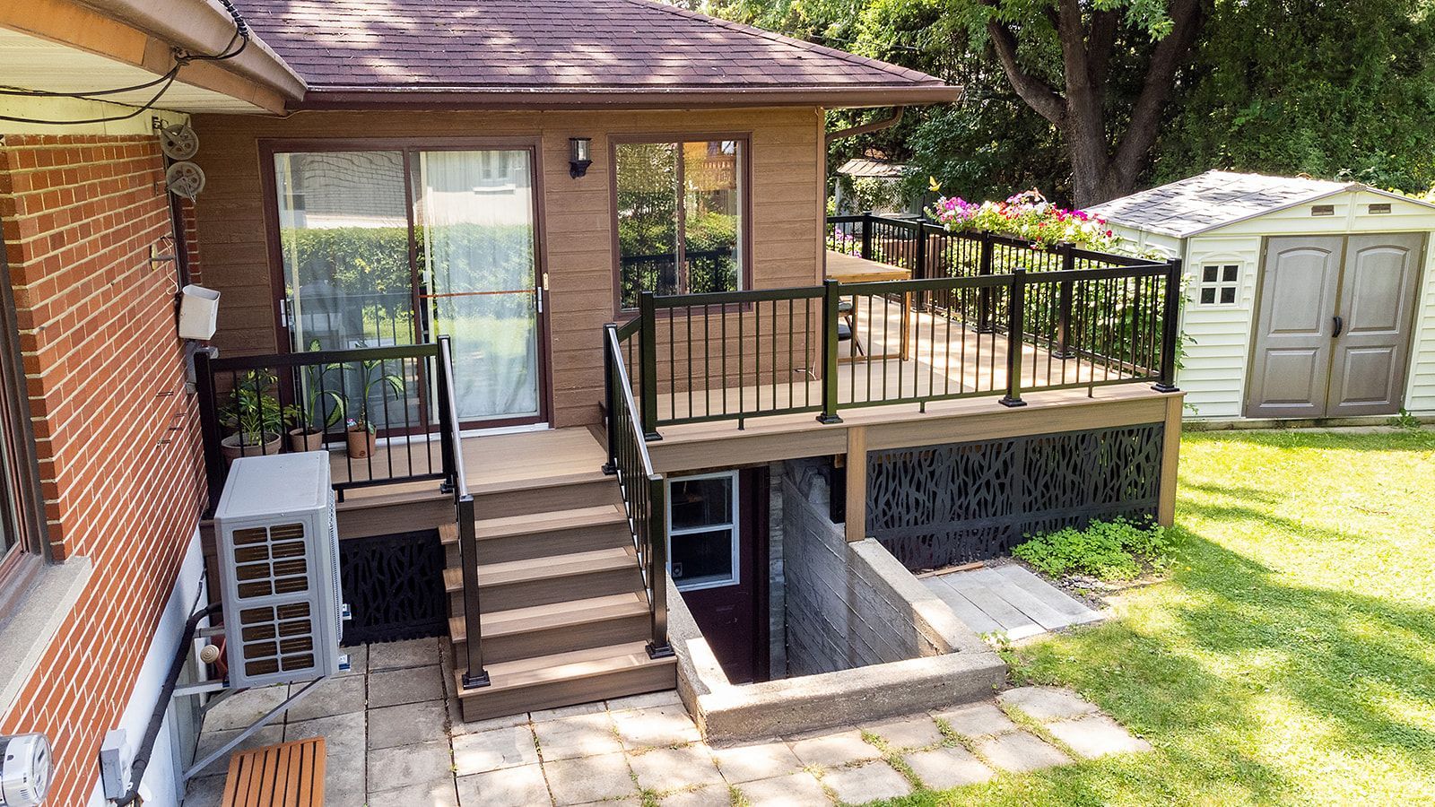 Terrasse arrière avec escalier menant à une porte et à un accès au niveau inférieur. Terrasse marron, abri de jardin et pelouse verte.