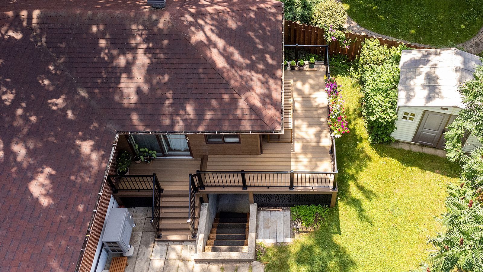 Vue aérienne d'une maison avec toit marron, terrasse en bois, escalier et pelouse verte.