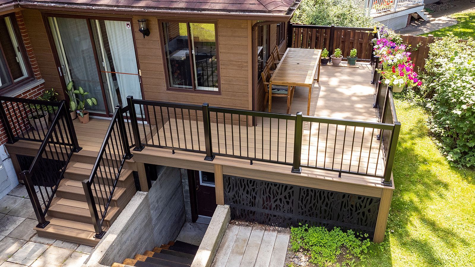 Terrasse en bois avec rambarde noire, donnant sur un jardin avec une table et des plantes.