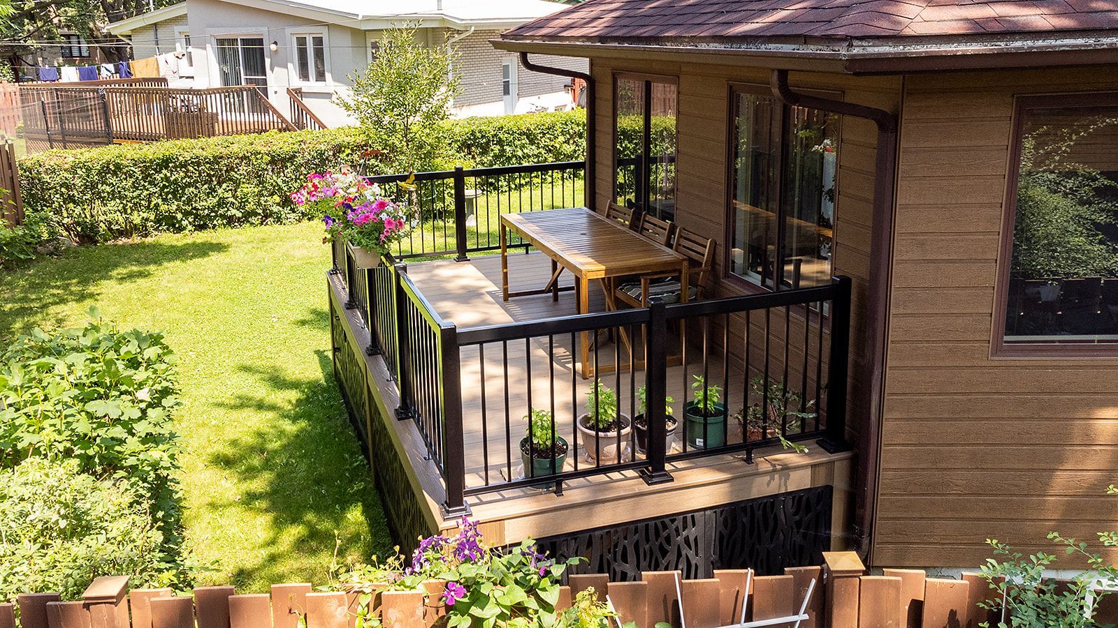 Terrasse en bois avec rambarde noire, table et chaises. Donne sur un jardin gazonné.