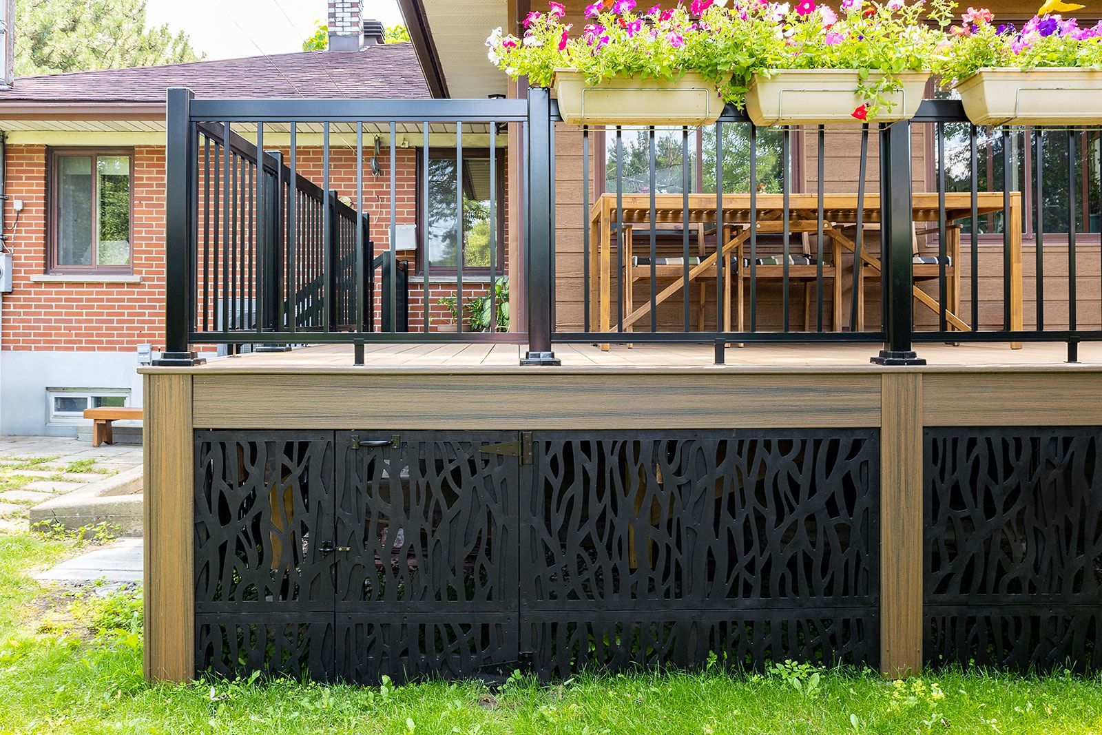 Terrasse avec rambarde noire, plinthes décoratives noires et jardinières ; planches de terrasse brunes et maison en briques en arrière-plan.