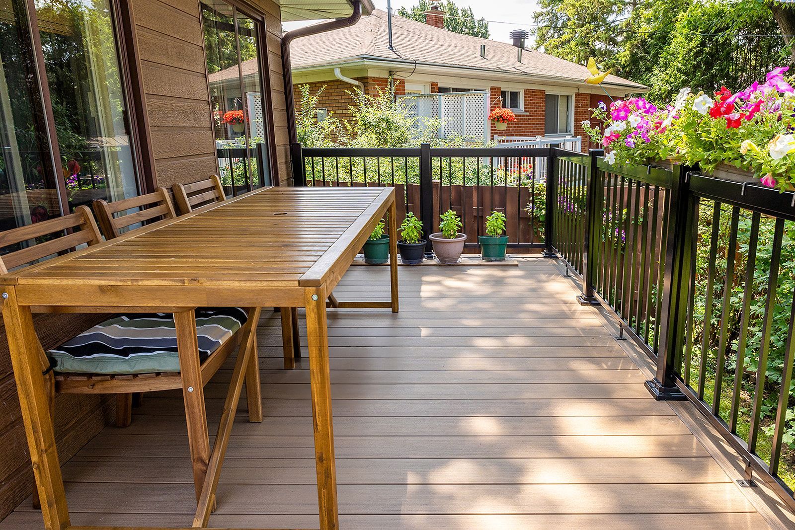 Terrasse en bois avec table et chaises, rambarde noire et jardinières.
