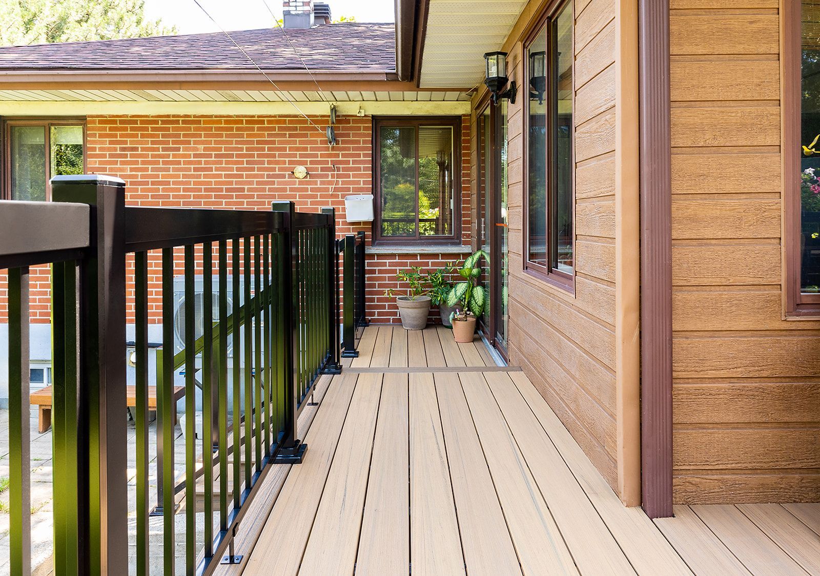 Terrasse en bois avec rambarde noire jouxtant une maison en briques.