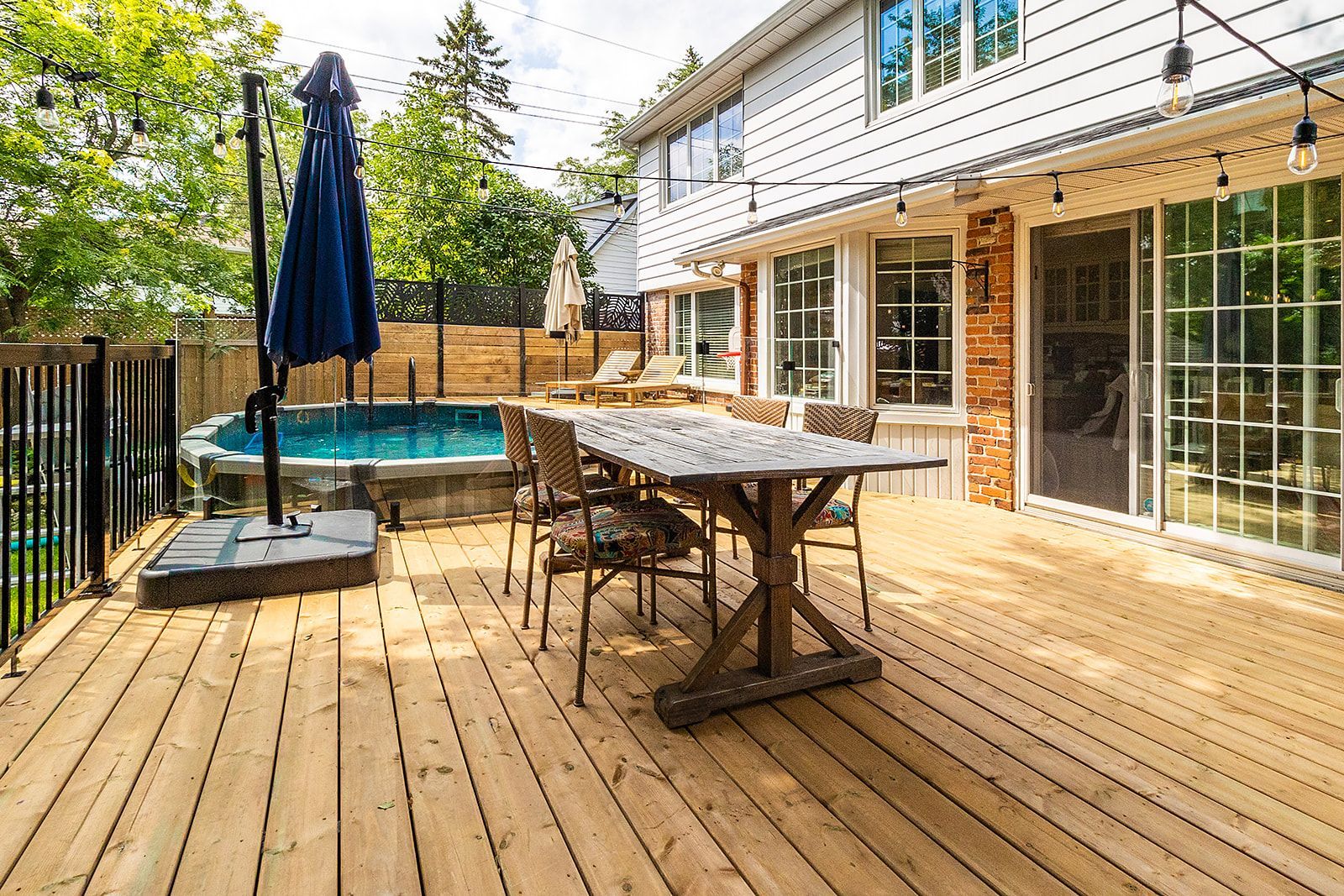 Terrasse en bois avec coin repas extérieur et petite piscine à côté d'une maison blanche avec portes coulissantes en verre.