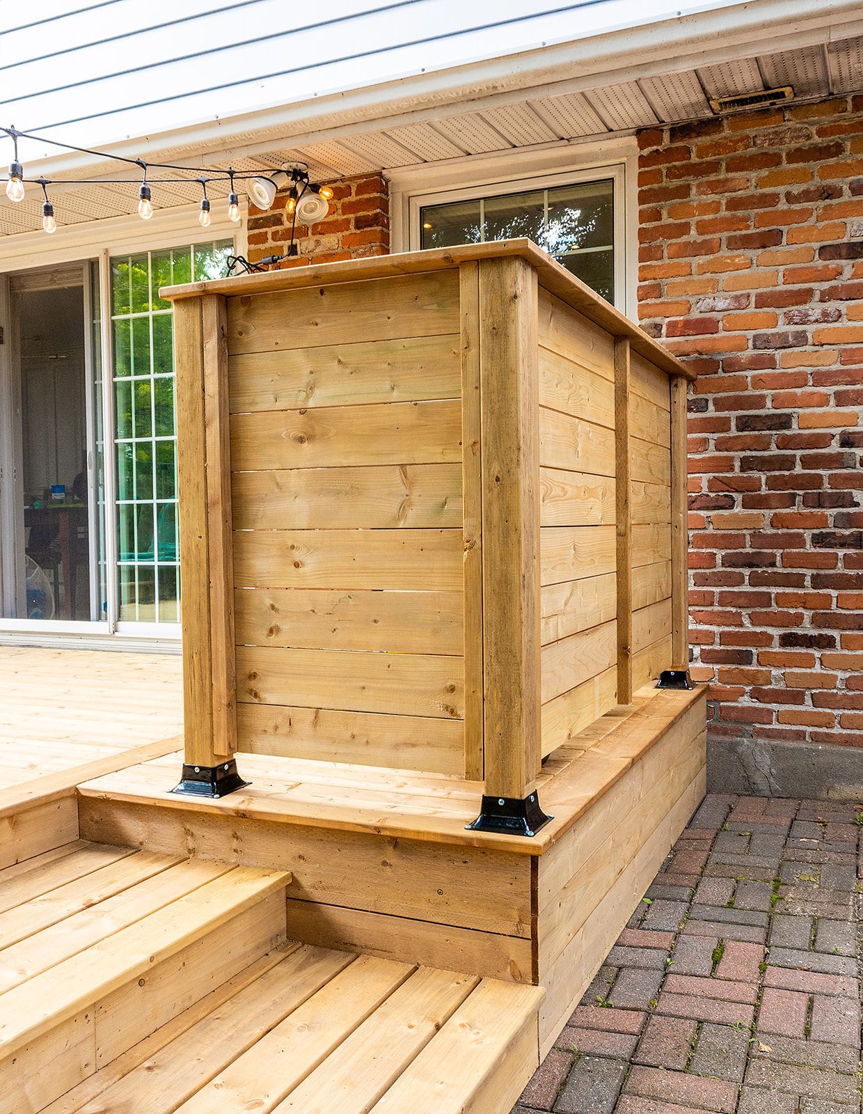 Terrasse en bois avec rambarde intégrée, jouxtant un mur de briques et une porte coulissante en verre.