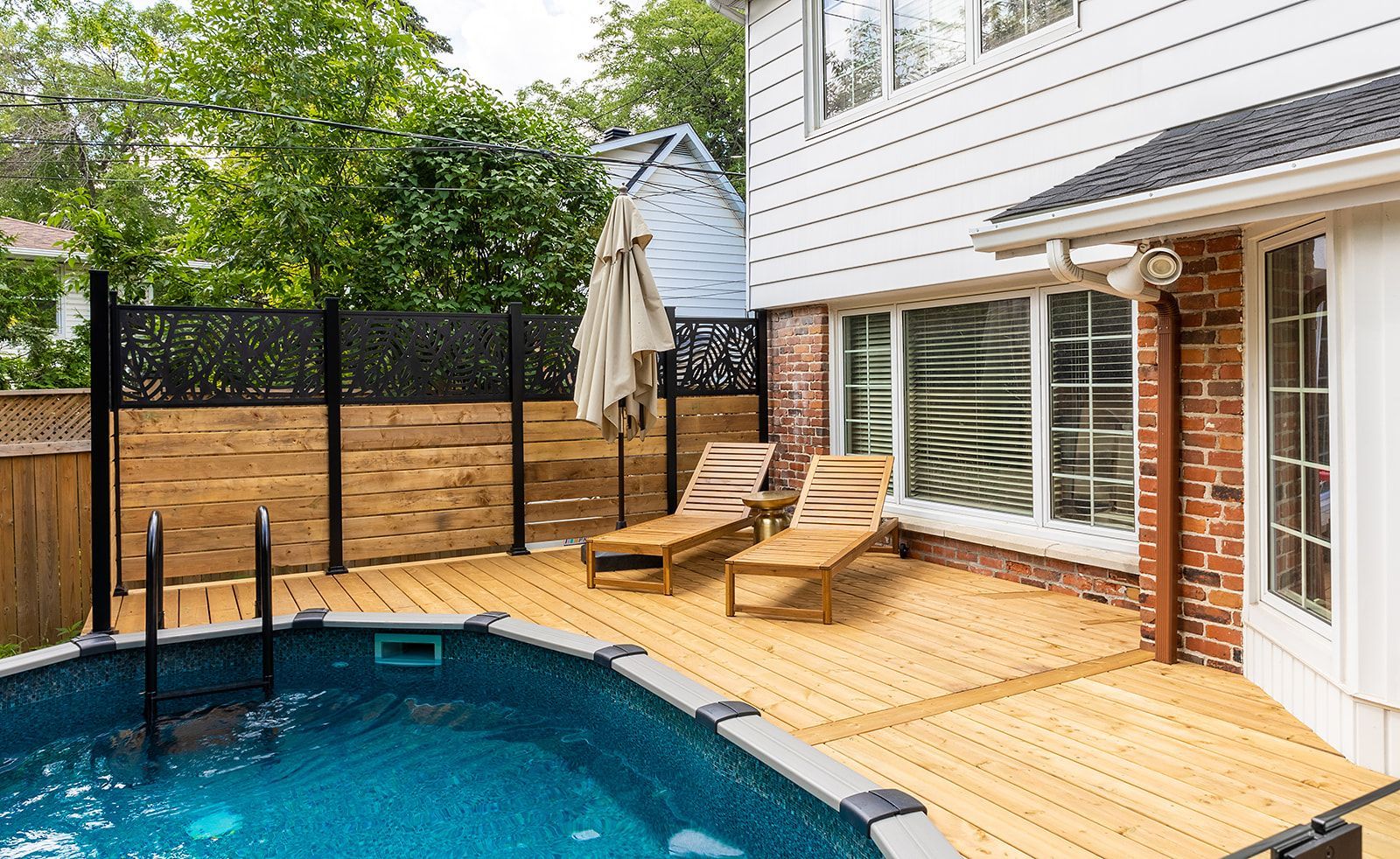 Cour arrière avec piscine hors sol, terrasse en bois, chaises longues et clôture décorative pour plus d'intimité, jouxtant une maison.