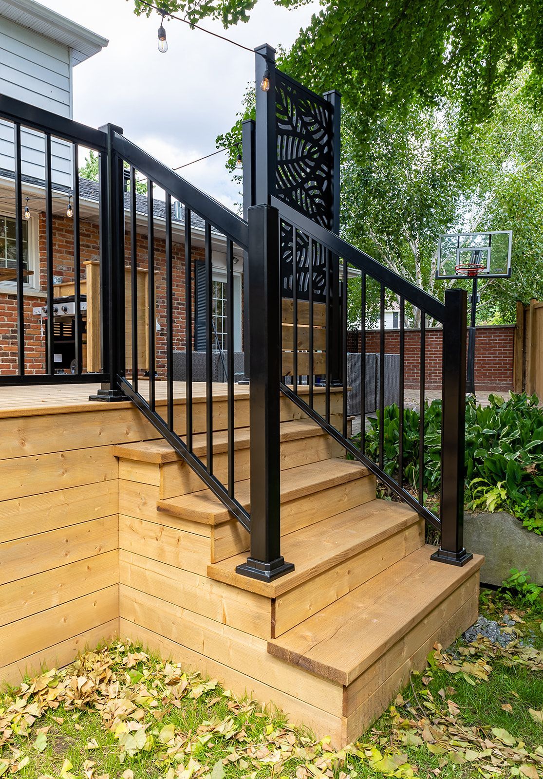 Terrasse en bois avec rambarde et marches noires, menant à une maison.