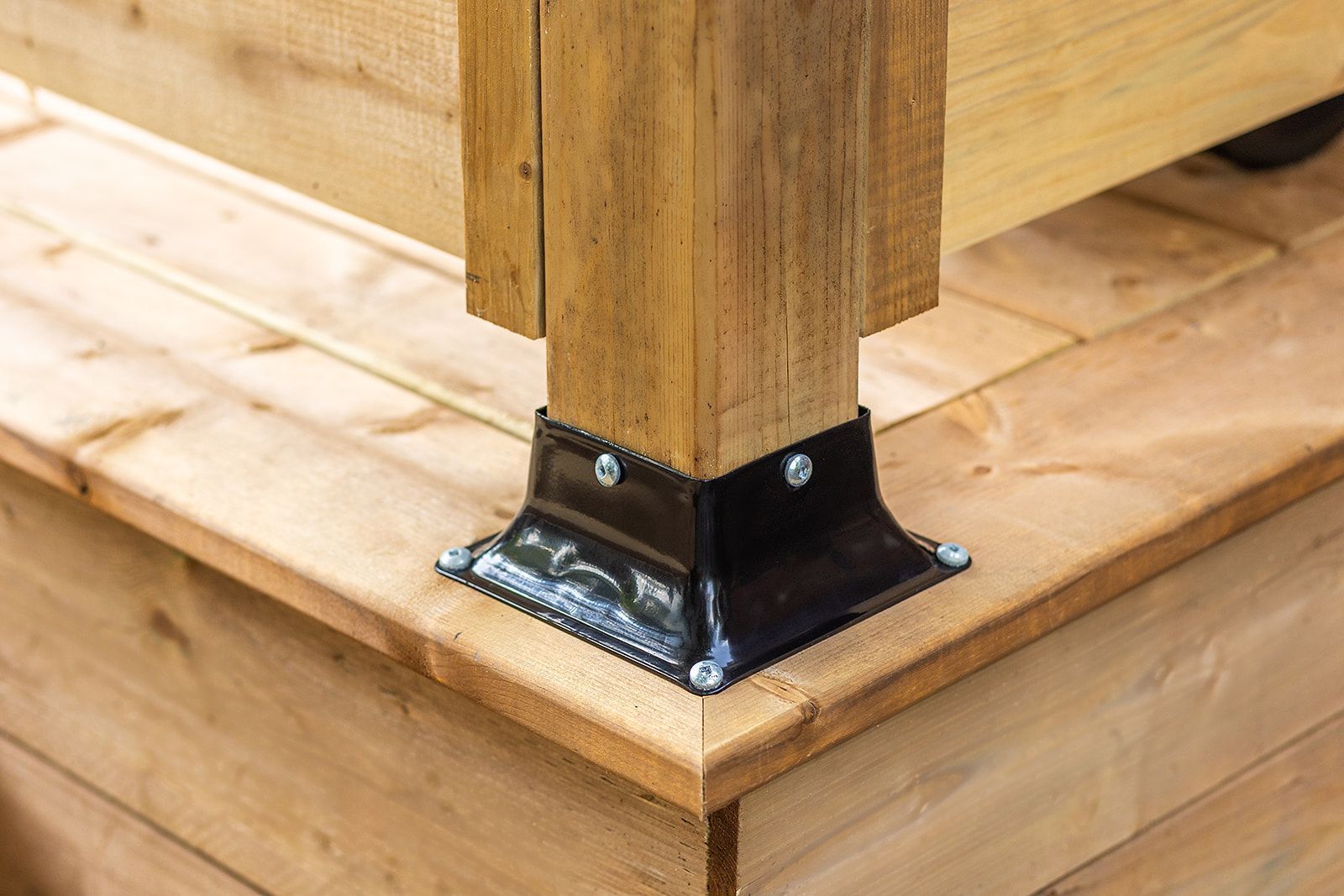 Base de poteau en métal noir fixant un poteau en bois à une terrasse en bois.