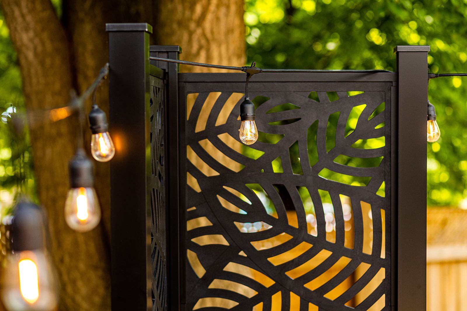 Paravent en métal noir avec découpes en forme de feuilles, éclairage chaleureux en extérieur.