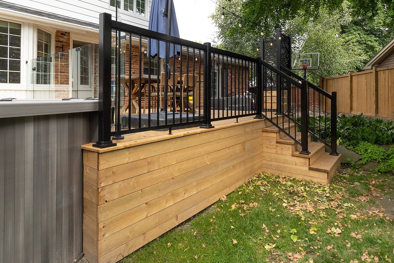 Terrasse et marches en bois avec rambarde noire, dans un jardin gazonné.