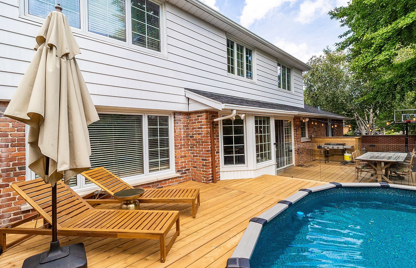 Jardin avec terrasse, piscine, chaises longues et maison à deux étages avec revêtement en briques.