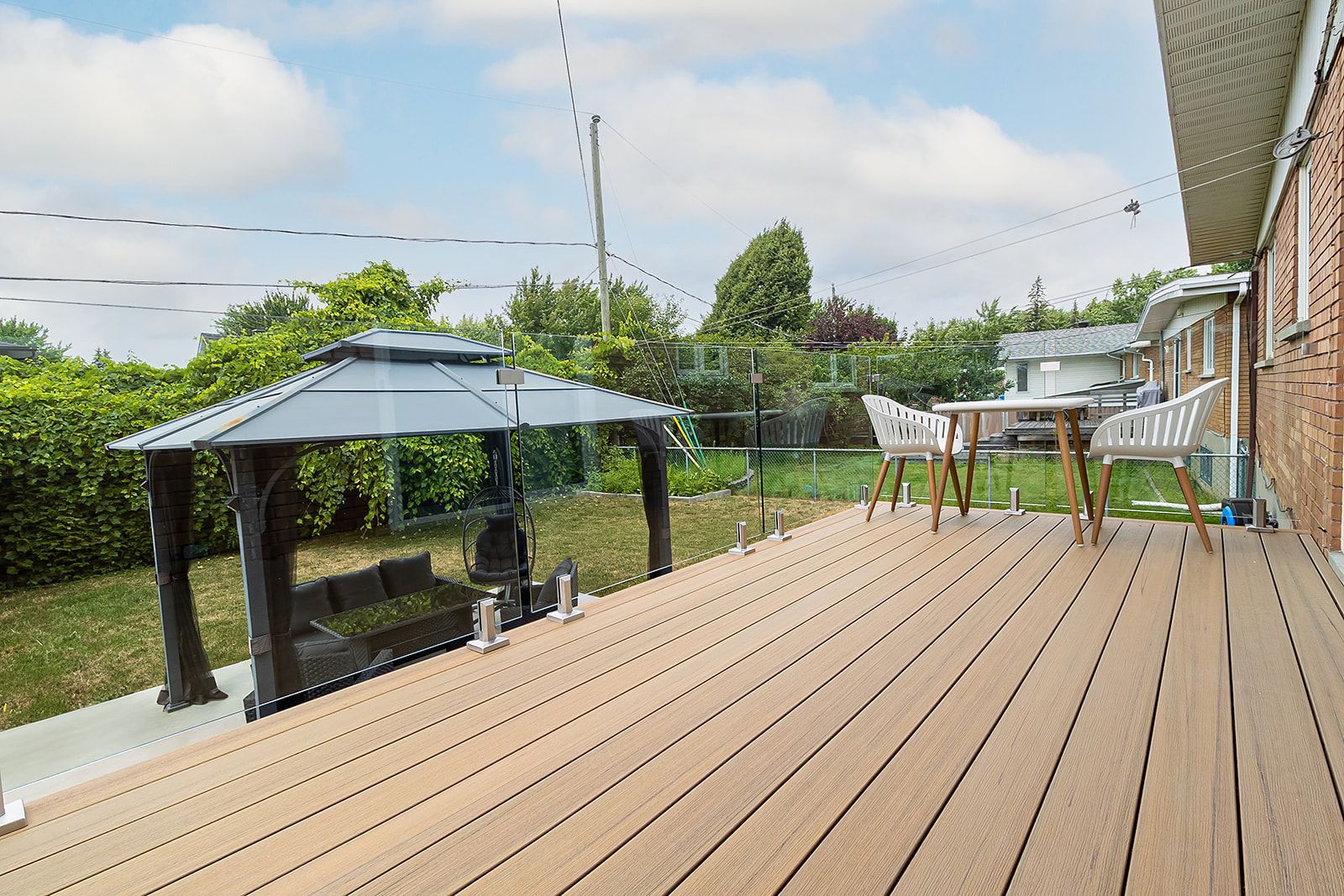 Terrasse arrière avec gazebo, table, chaises et maison en briques. Pelouse verte et arbres en arrière-plan.