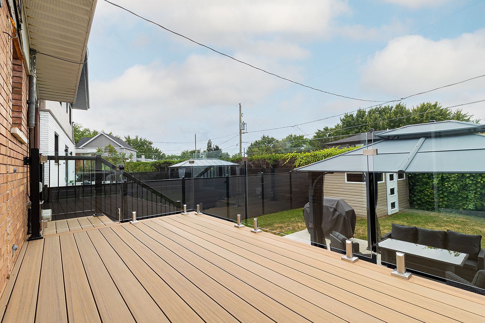 Terrasse arrière avec planches composites brunes, un gazebo et des guirlandes lumineuses.
